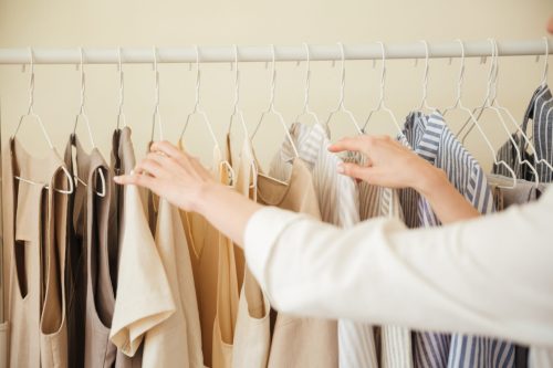Close up of woman hands choosing clothes hanging on rack in workshop